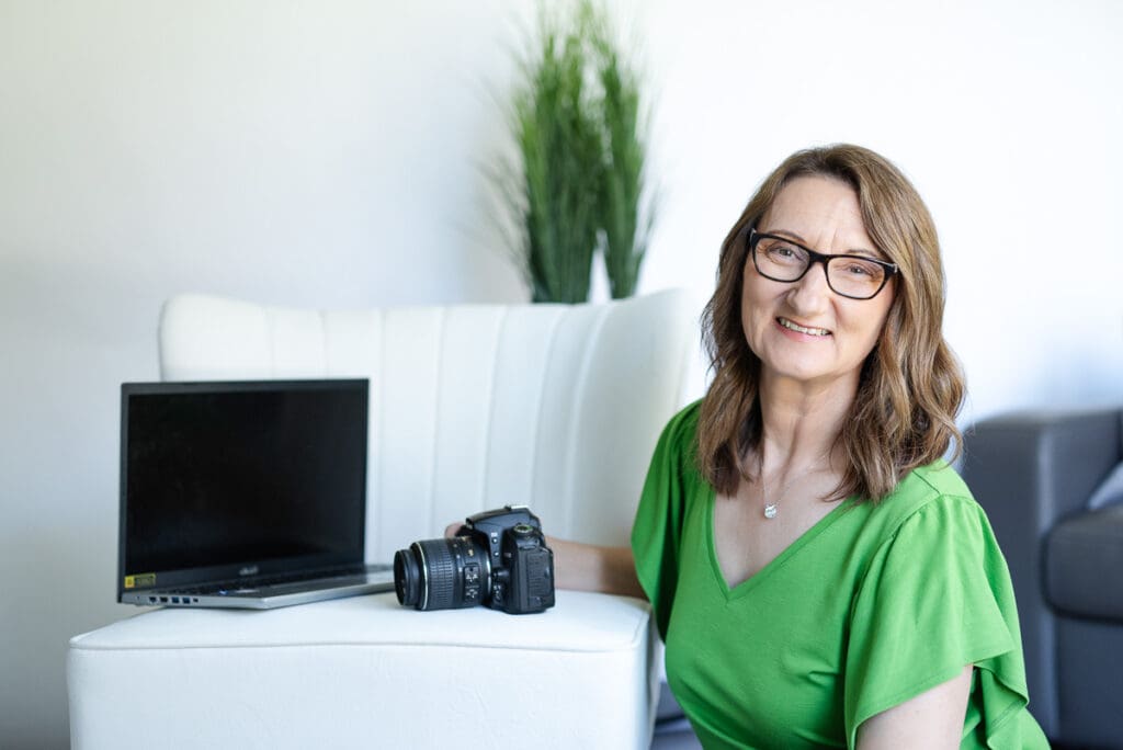 Lisa from Lisa Q Photography smiling at camera with a camera and laptop next to her.