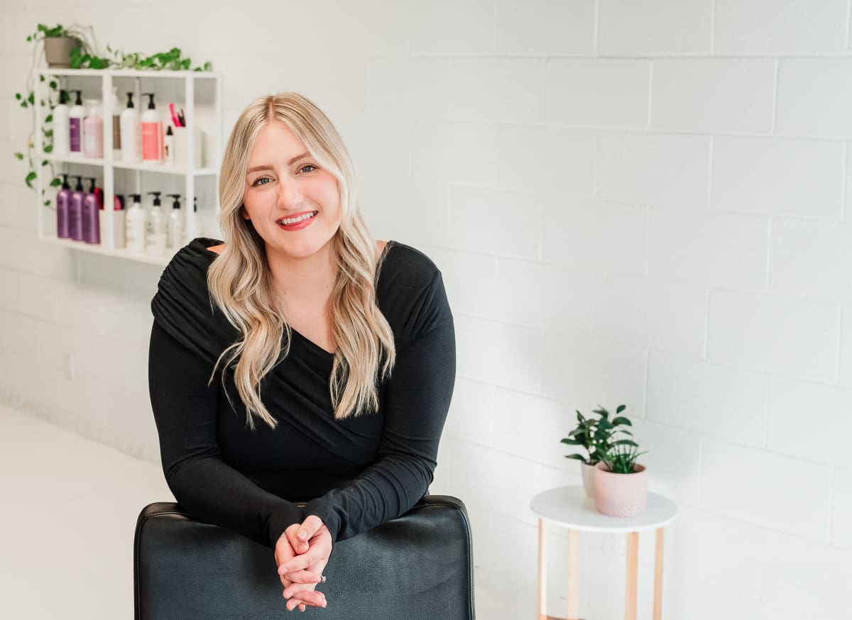 Brand photo of salon owner smiling warmly in bright, clean, modern salon space.