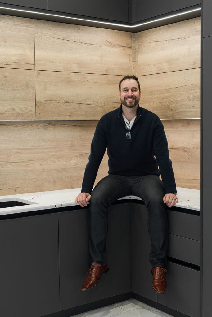 Dale sitting in modern kitchen in the showroom at The Cabinet Mill at brand photo session